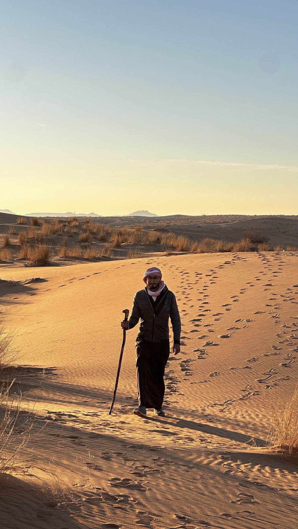 Aziz walking across desert dunes at sunset wearing a shemagh